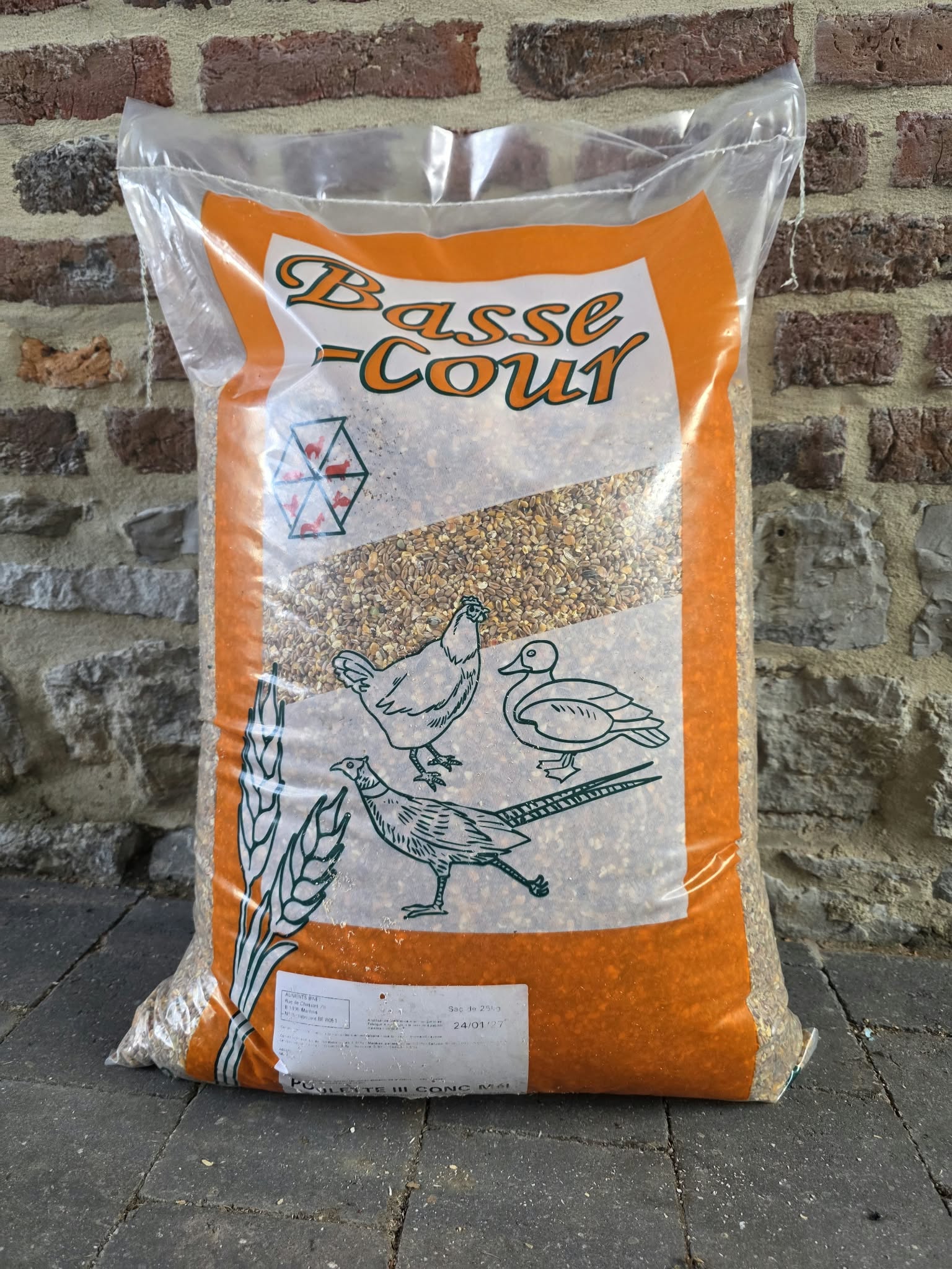 Sac orange de mélange concassé pour volailles, posé devant un mur de briques